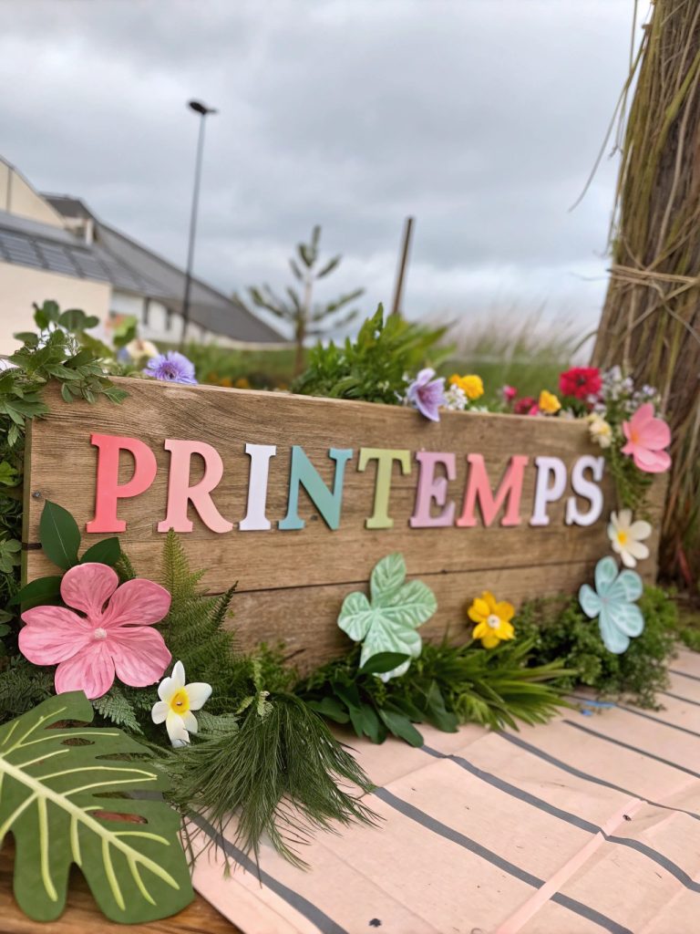 Tableau mural avec des lettres en bois formant le mot 'Printemps', entouré de fleurs artificielles et de feuillages